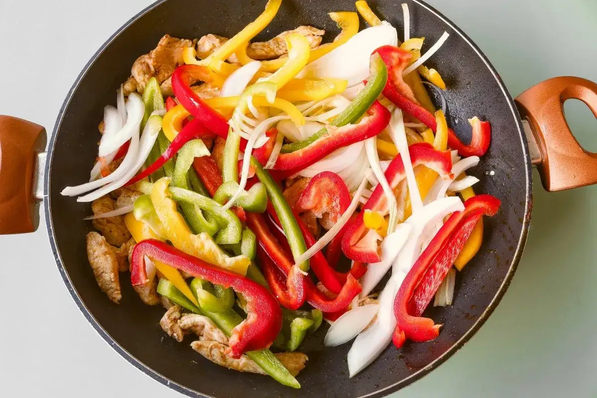 Fajitas de pollo en sartén con pimientos de colores y cebolla, listas para cocinar.