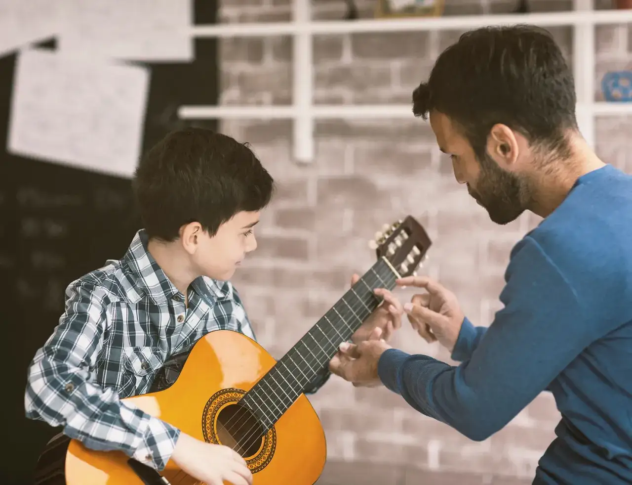 Ein Mann zeigt einem Jungen, wie man Gitarre spielt. Er erklärt, was ein Metronom ist, um den Rhythmus zu halten.