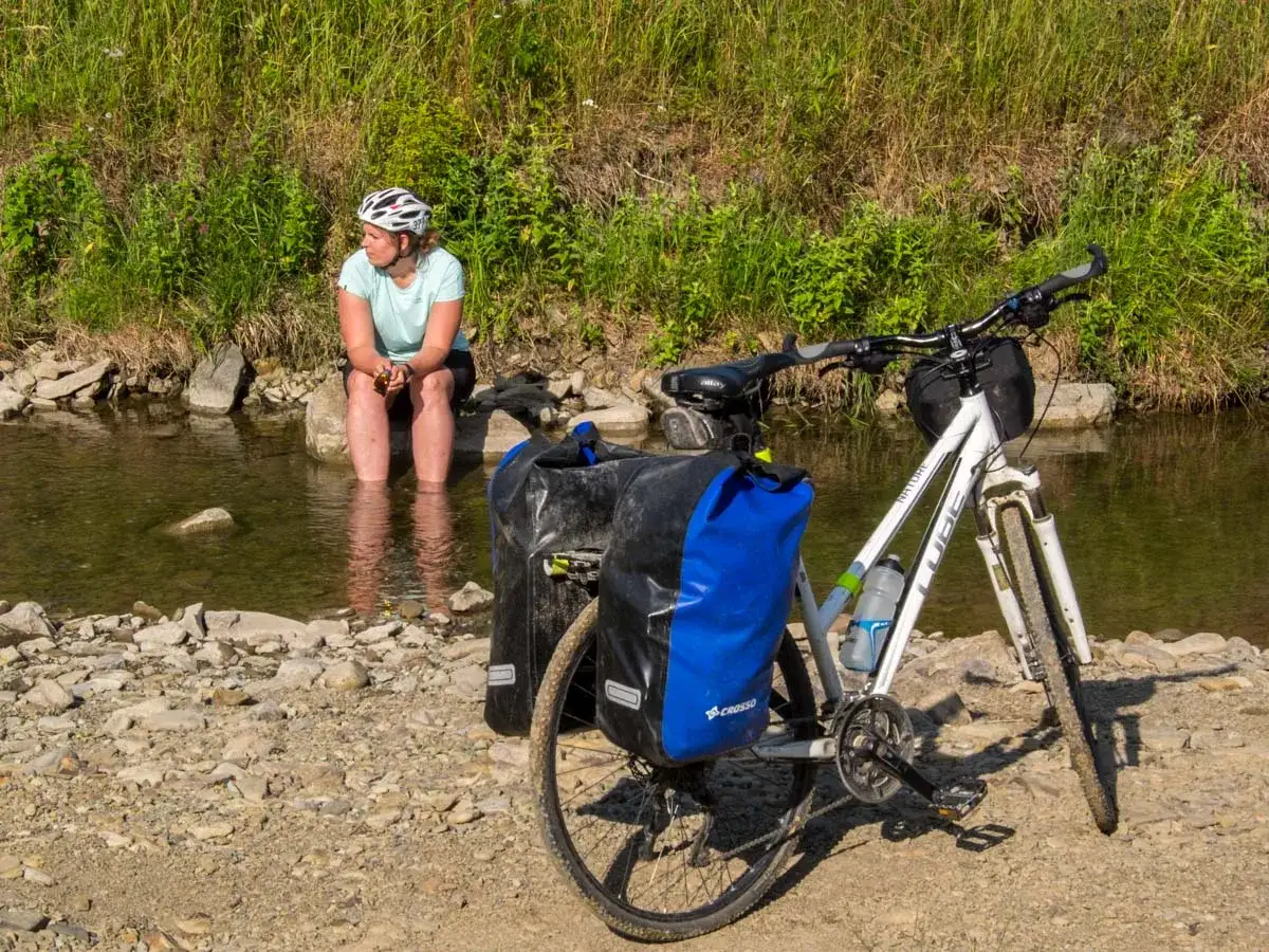 Kobieta w kasku odpoczywa nad wodą, zanurzając stopy. Obok rower z sakwami, gotowy do dalszej podróży przez malowniczą dolinę Wisłoki.