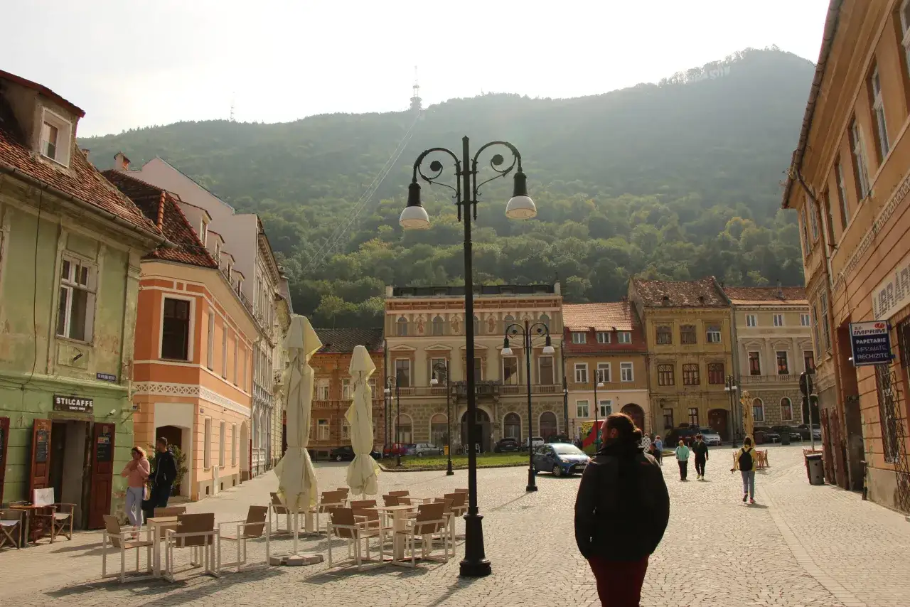 Spacer po urokliwym Brasov w Rumunii. Zabytkowe kamienice, kawiarniane stoliki i góra Tampa w tle.