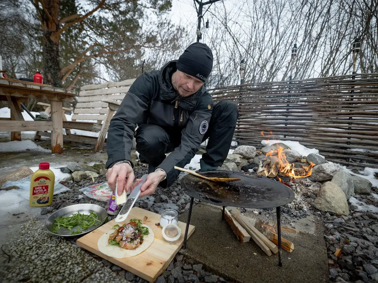 Man förbereder friluftsliv mat recept vid en eld. Han river ost över en tortilla med fyllning.