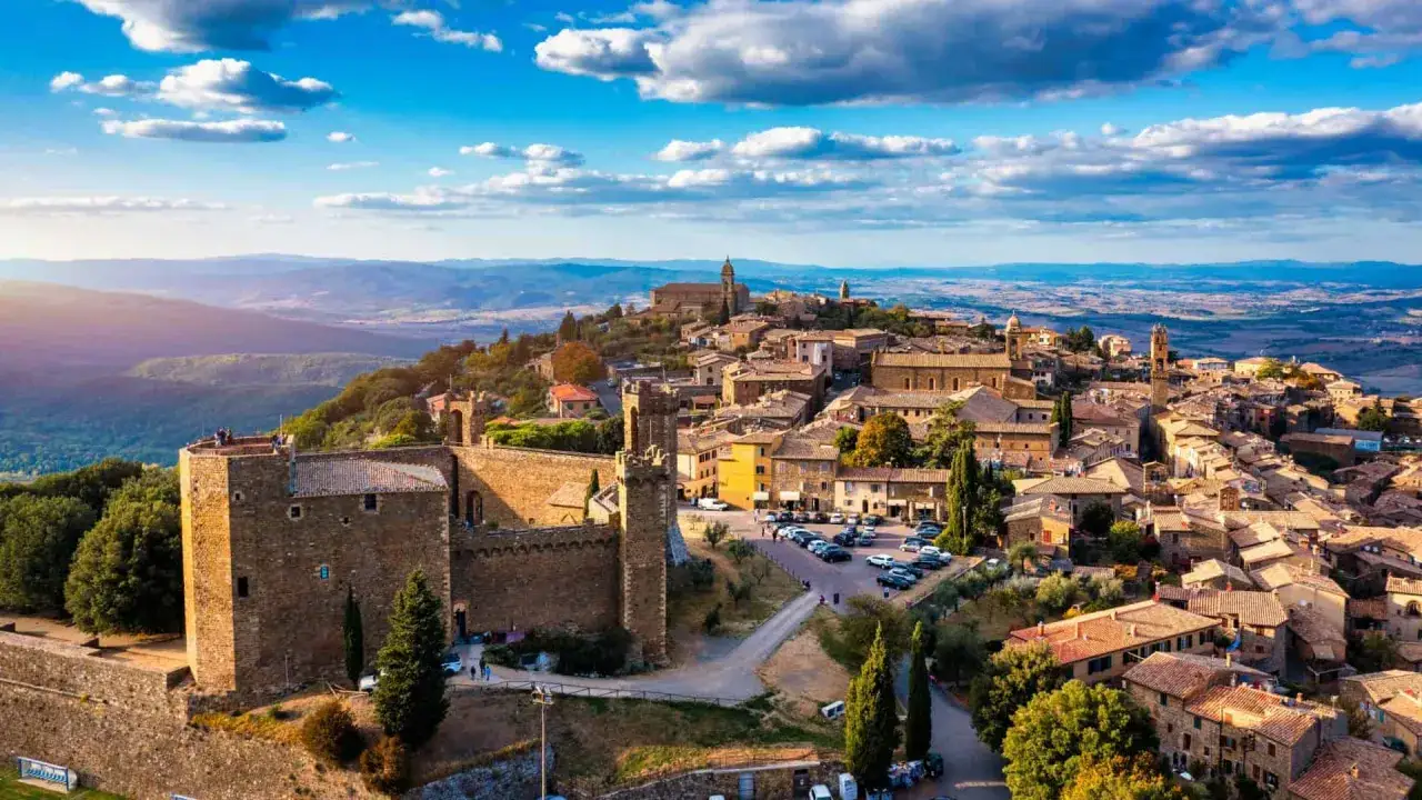 Un borgo medievale arroccato su una collina, tra i pi&ugrave; belli d'Italia, con un castello imponente e case in pietra sotto un cielo azzurro.