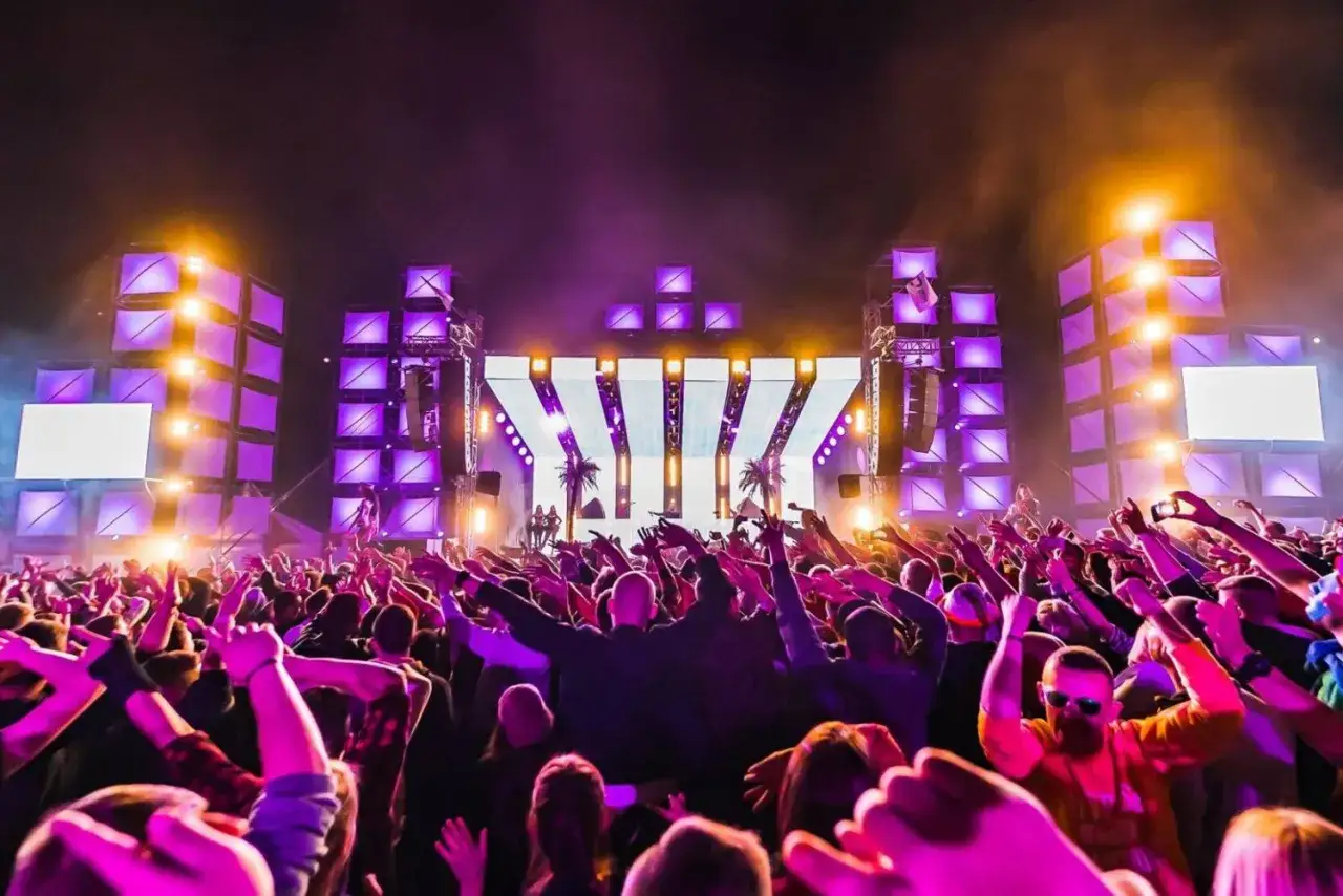 Tłum szaleje na trzcianka festiwal pod neonowym niebem. Kolorowe światła sceny i palmowe dekoracje tworzą magiczną atmosferę.