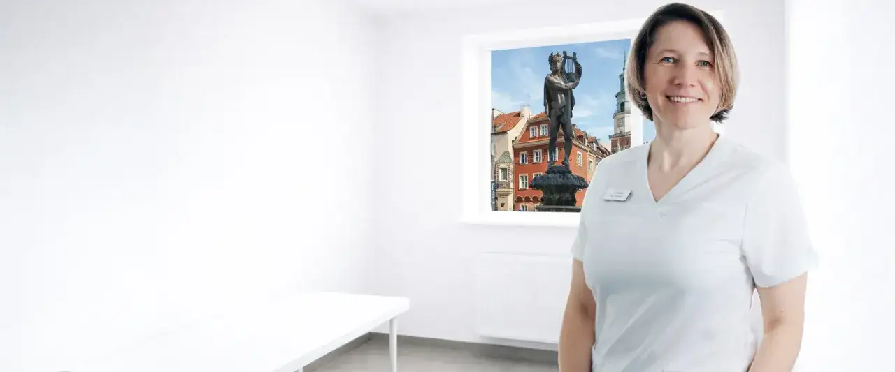 Uśmiechnięta lekarka w białym uniformie na tle okna z widokiem na poznański Stary Rynek.