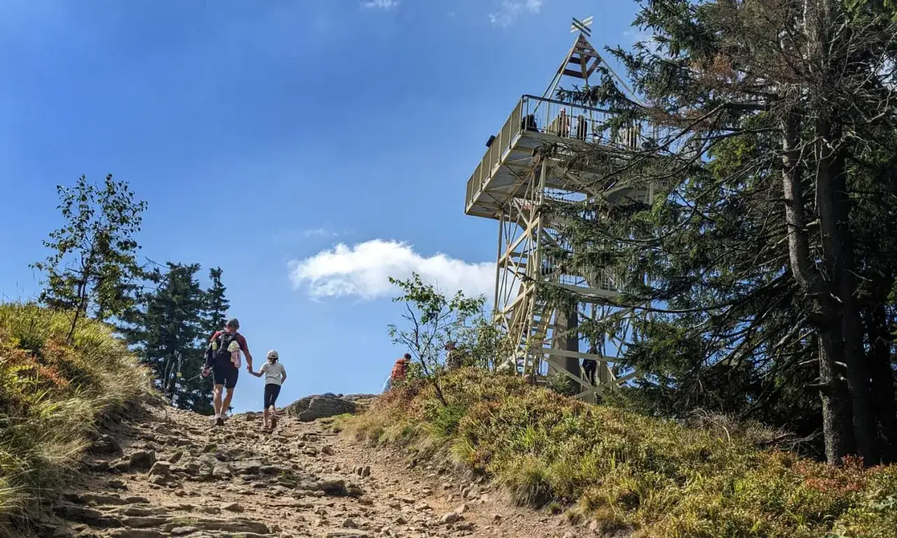 Rodzina wspina się kamienistym szlakiem na Baranią Górę, w tle widoczna wieża widokowa.
