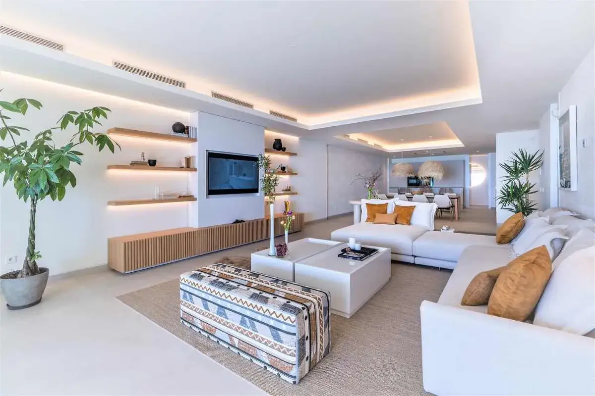 Elegante sala de estar con sofás blancos, mesa de centro moderna y estanterías flotantes. La decoración de casas es minimalista y luminosa, con toques de color en los cojines.