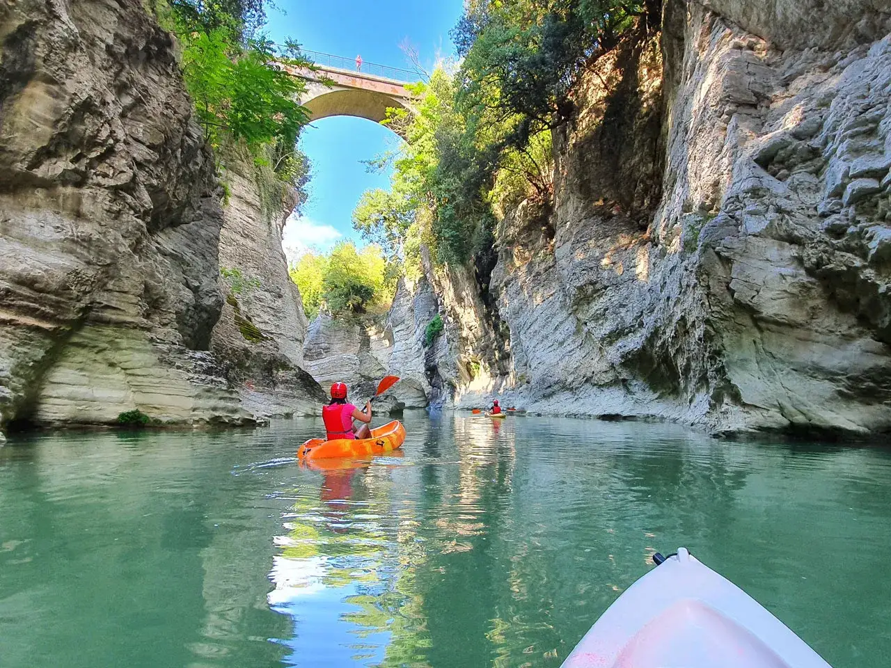 Kayak nel **canyon di Fossombrone**, tra alte pareti rocciose e un ponte ad arco.