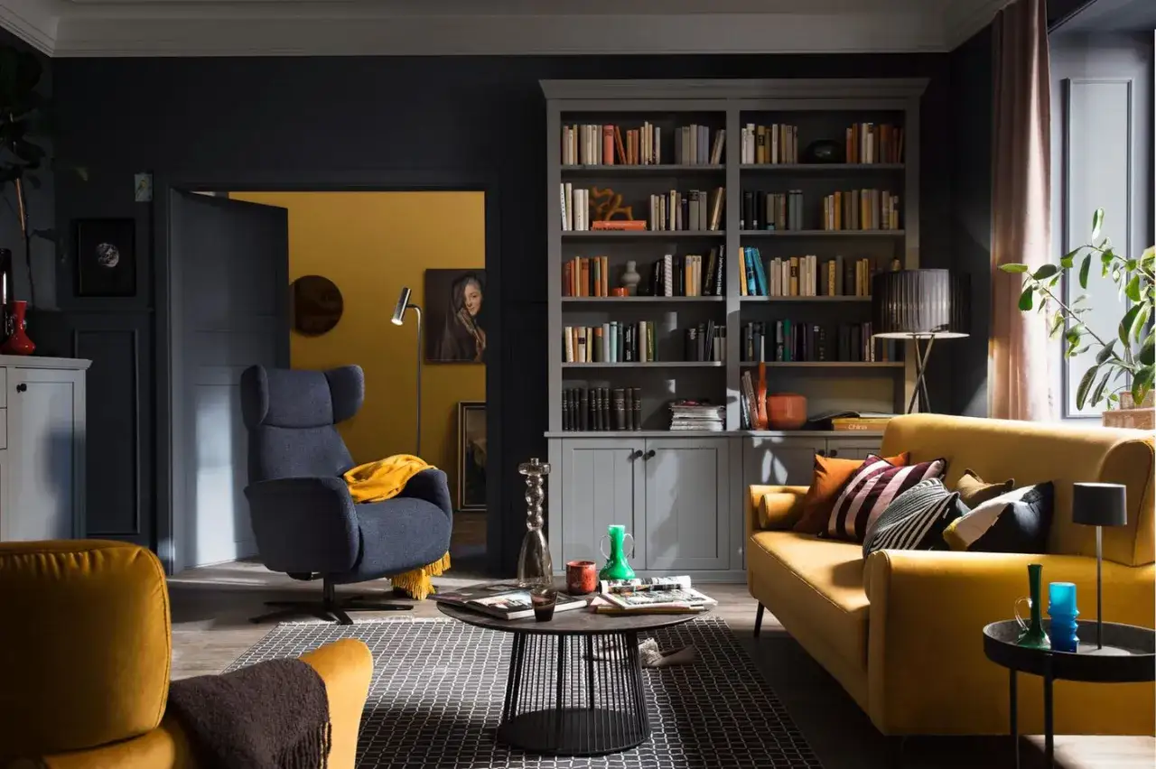 Gemütliches Wohnzimmer im englischen Landhausstil mit gelbem Sofa, dunklem Sessel und Bücherregal.
