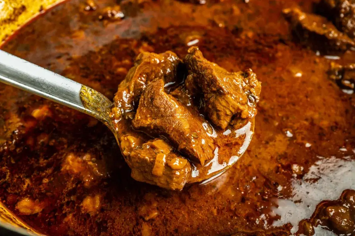 Ein L&ouml;ffel voller herzhaftem Wildschwein Gulasch, das in einer reichhaltigen, dunklen Sauce schmort.