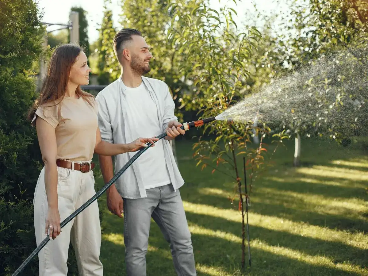 Pareja riega el jardín. La manguera de riego, de medidas estándar, rocía agua sobre la vegetación.