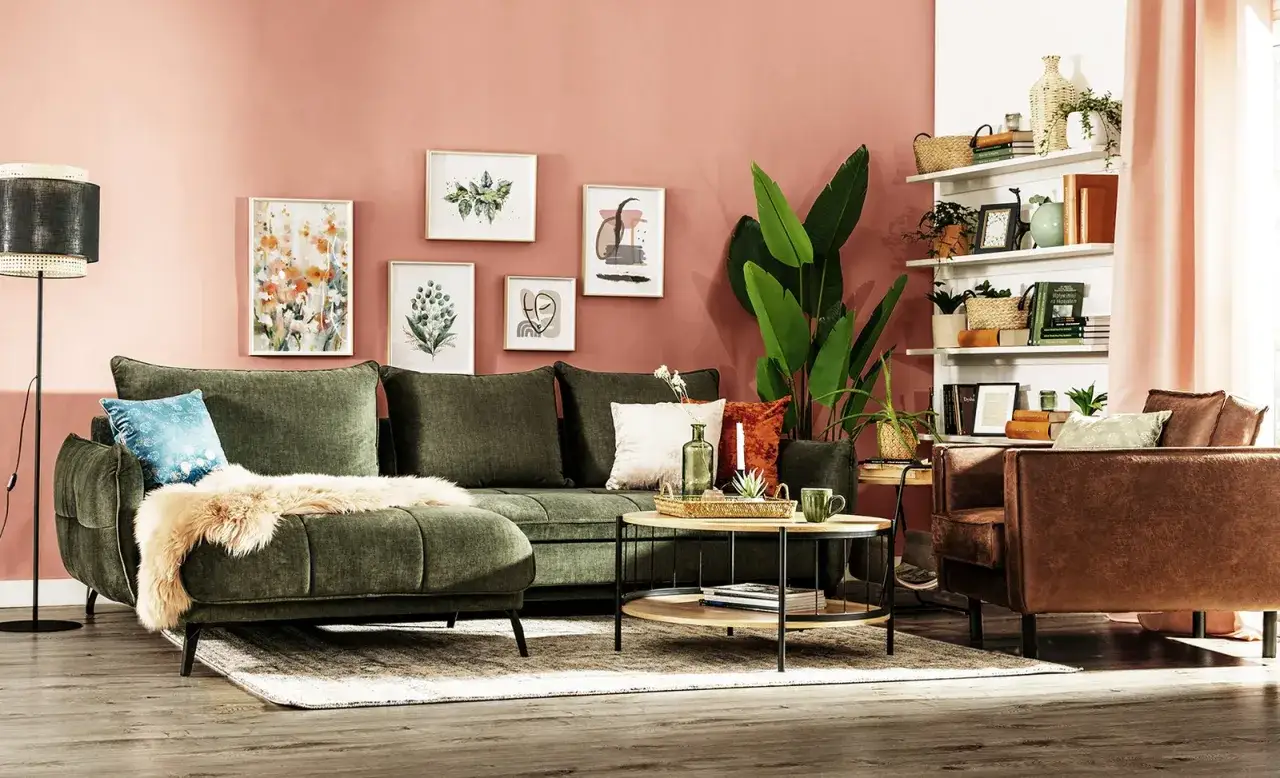 Zielony salon inspiracje: wygodna, oliwkowa sofa, brązowy fotel, stolik kawowy, rośliny i obrazy na różowej ścianie.