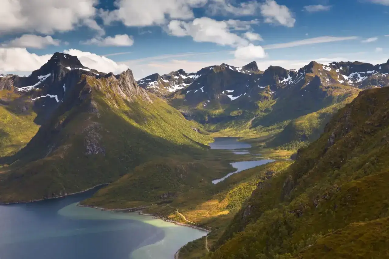 Vandra i Norge genom dramatiska fjordlandskap med snöklädda berg, gröna dalar och glittrande sjöar under en molnig himmel.