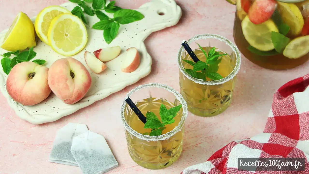 Deux verres de thé glacé maison, décorés de menthe fraîche et de sucre, accompagnés de pêches plates, de citrons et de sachets de thé.