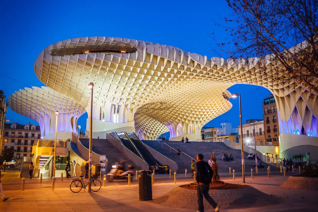 Las estatuas en Sevilla no son lo único impresionante. La arquitectura moderna de Las Setas ilumina la noche, con gente paseando y disfrutando.