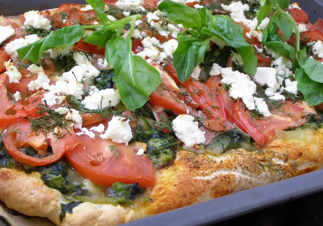Pyszna pizza z fetą, pomidorami i świeżą bazylią, posypana koperkiem. Idealna na letni wieczór.