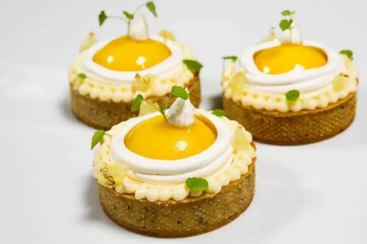 Trois tartelettes citronnées surmontées d'une délicate meringue italienne, garnies de fruits et de feuilles vertes.