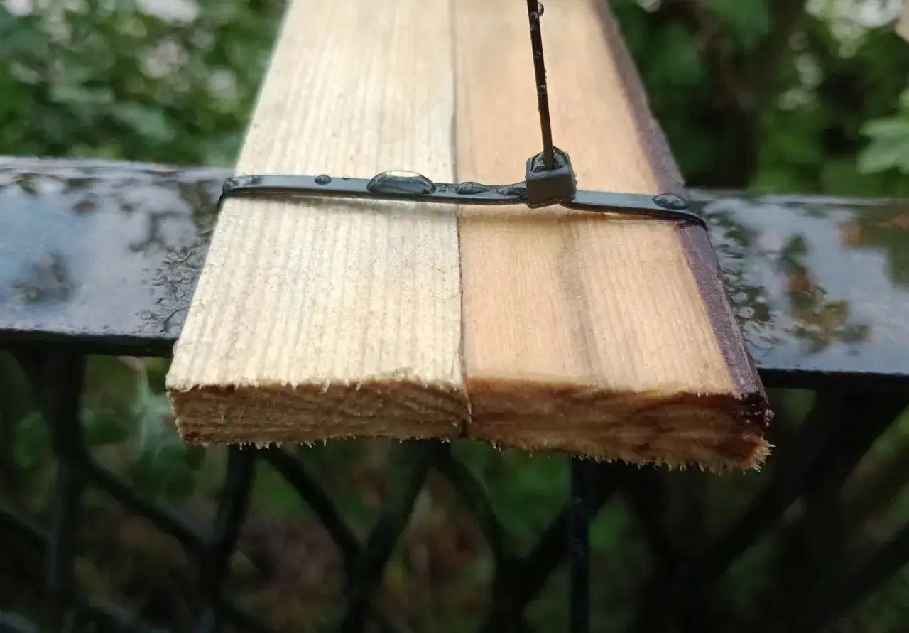 Test zabezpieczenia sklejki przed warunkami atmosferycznymi. Jedna połowa deski jest surowa, druga zabezpieczona ciemnym impregnatem, chroniącym przed wilgociącią.