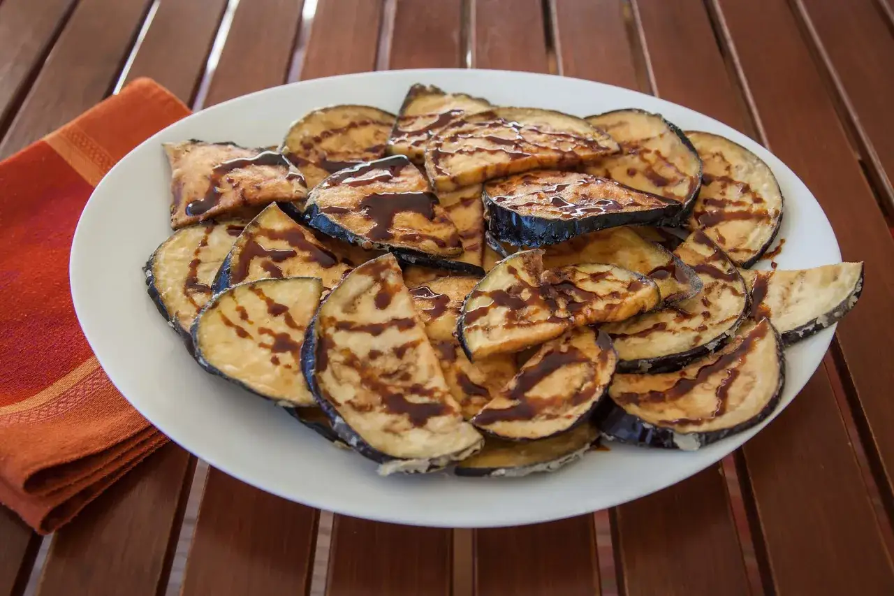 Berenjenas rebozadas con miel, doradas y crujientes, servidas en un plato blanco sobre una mesa de madera.