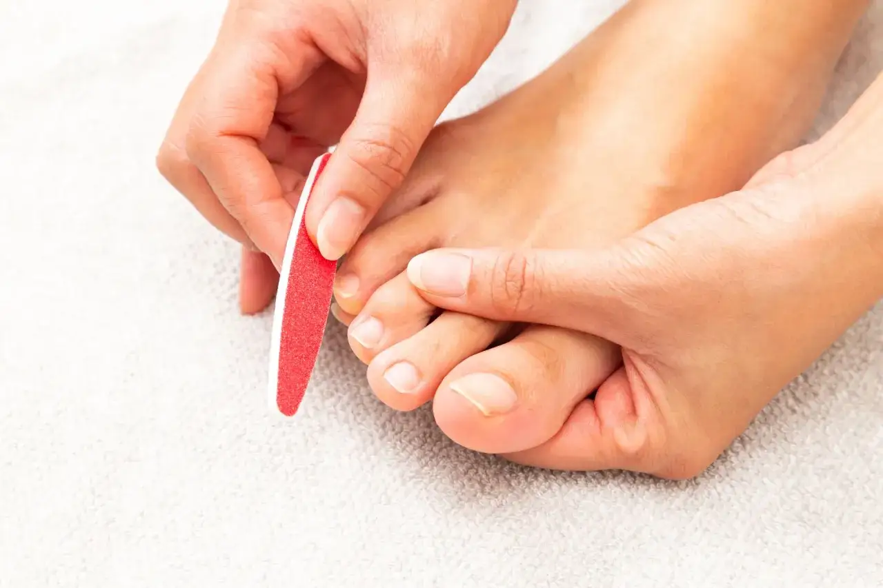 Dłonie delikatnie opiłowują paznokcie u stóp, przygotowując je do zabiegu pedicure japoński.