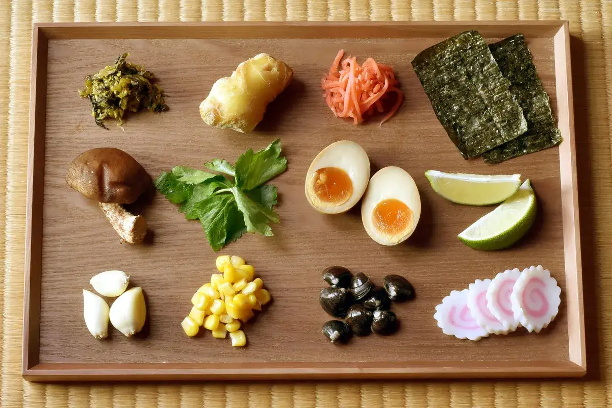 Eine Auswahl an k&ouml;stlichen Ramen-Toppings: eingelegter Ingwer, Shiitake-Pilz, Ei, Mais, Nori, Limette, Knoblauch, Muscheln und Fischkuchen.