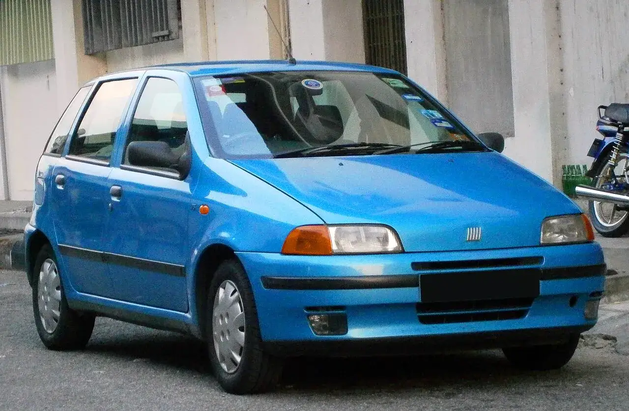 Una Fiat Punto blu brillante parcheggiata in strada, con un motorino sullo sfondo.