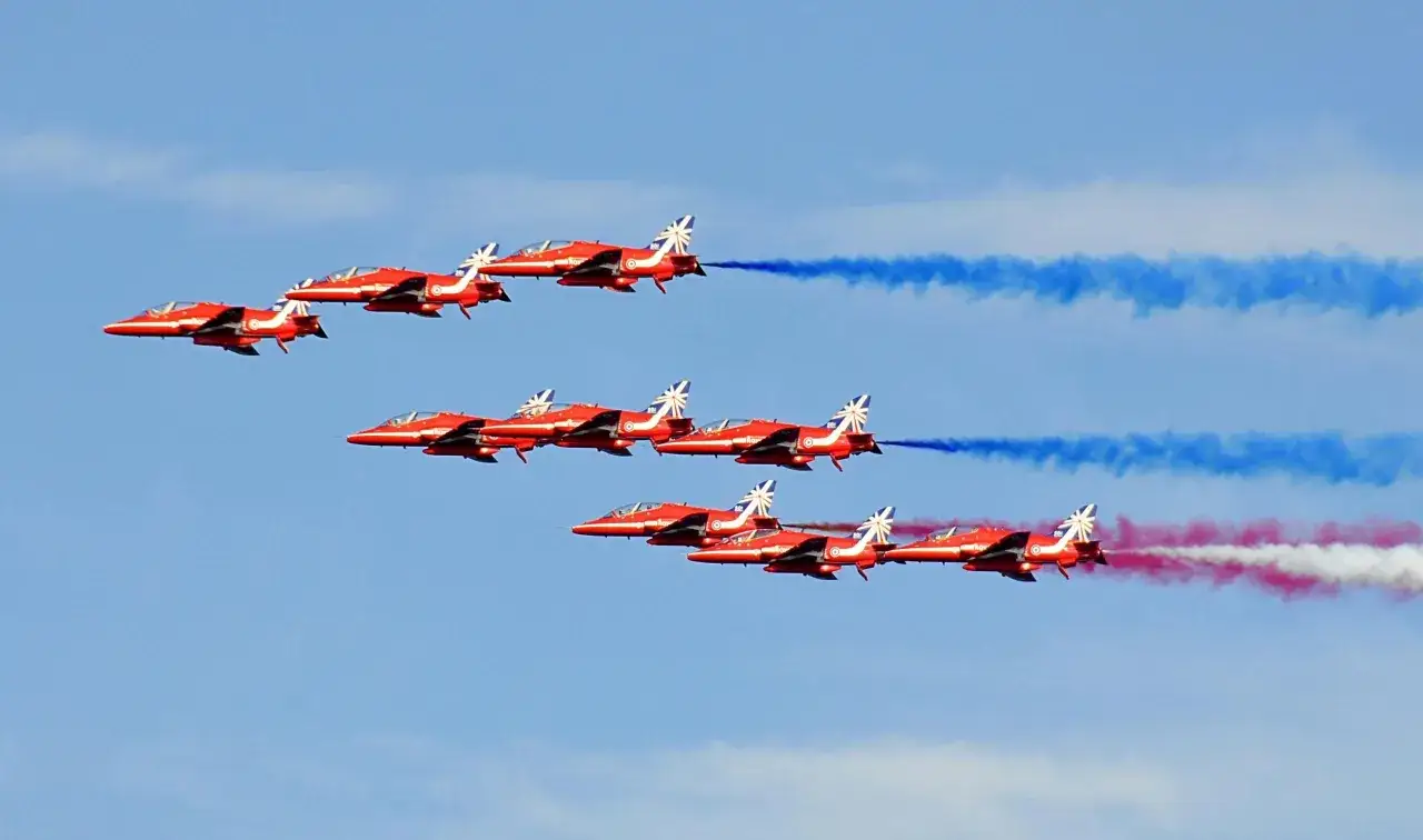 Une formation d'avions rouges en plein vol, laissant des traînées de fumée bleue et rouge dans le ciel.