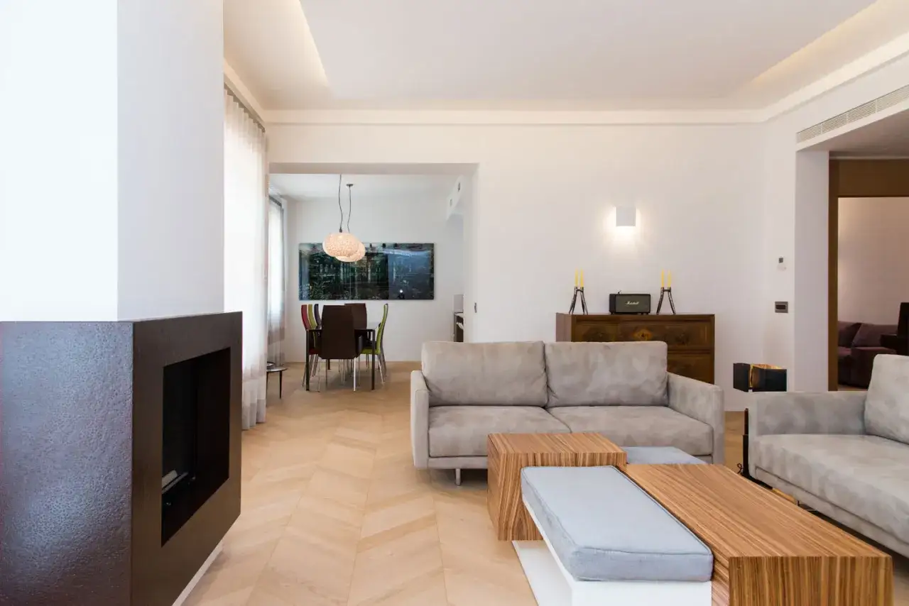 Soggiorno moderno con camino, divani grigi e parquet spina di pesce. Pro e contro di questo elegante pavimento in legno.