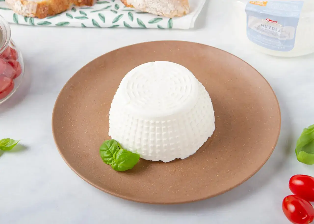 Ricotta di mucca fresca su piatto marrone, con basilico e pomodorini. Ideale per un pasto leggero, con poche calorie.