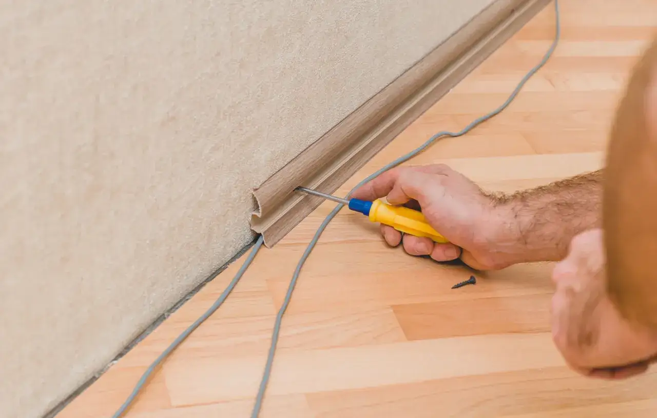 Mann schraubt Sockelleiste an, um Kabel zu verstecken. Gute kabel verstecken ideen für ein sauberes Zuhause.
