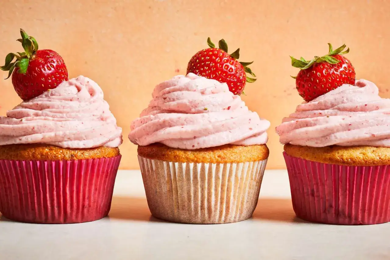 Drei Erdbeer-Cupcakes mit rosa Frosting und frischen Erdbeeren obendrauf.