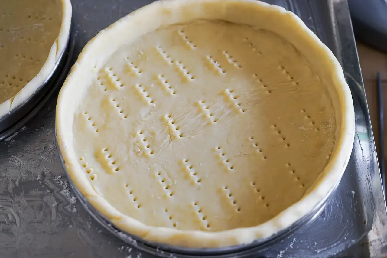 Pâte sablée prête à cuire pour un fond de tarte, piquée de trous pour une cuisson parfaite.