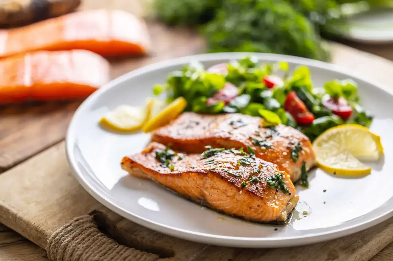 Salmone cotto con erbe e limone, accompagnato da insalata fresca. Un pasto gustoso per chi vuole aumentare il metabolismo.