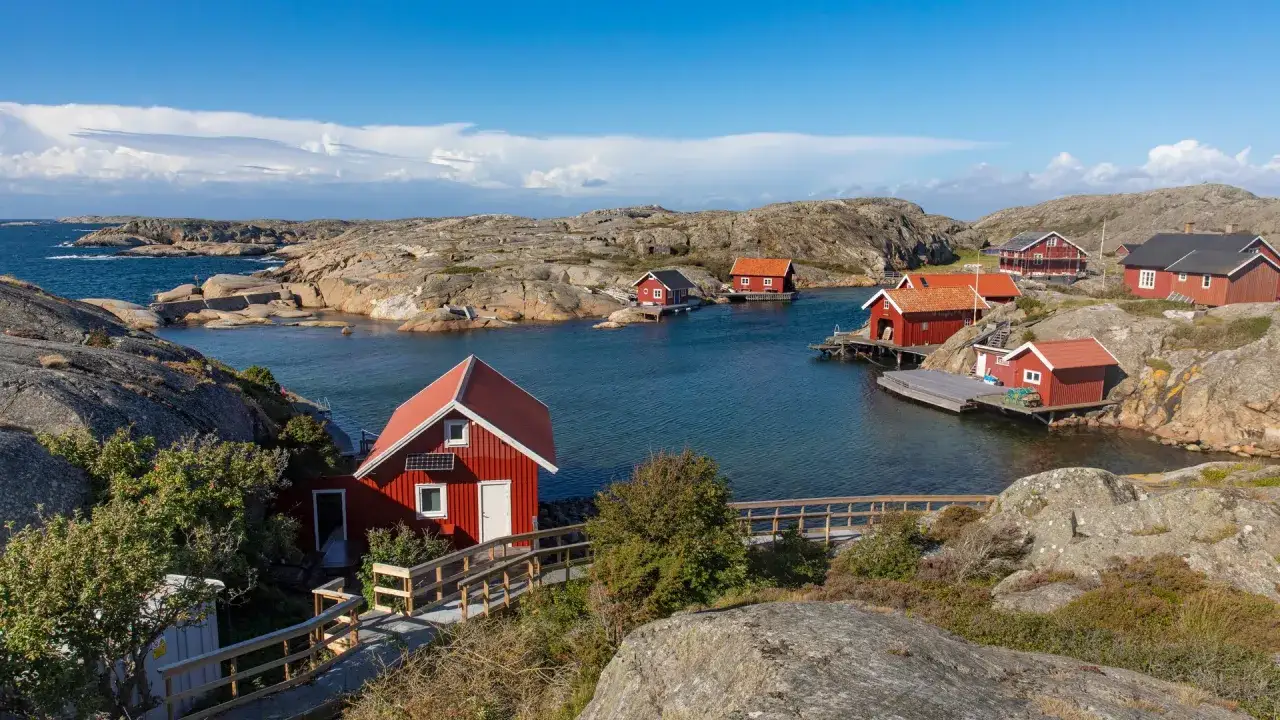 Röda stugor vid en vik i Sverige. Perfekt för vandringsresor singel, med klippor och blått hav.