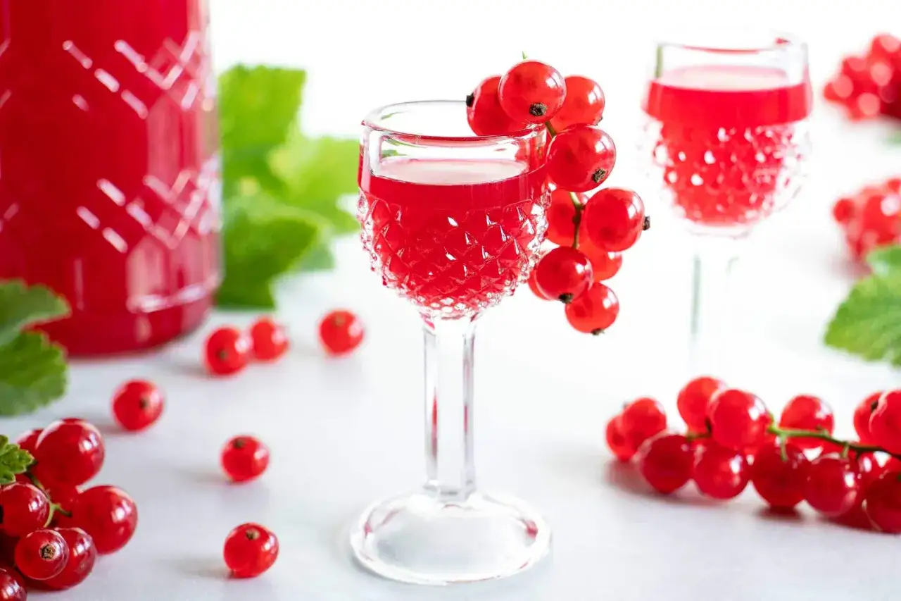 Rote Johannisbeeren schnaps ansetzen: Ein Glas mit rotem Lik&ouml;r, garniert mit frischen Beeren, daneben eine Flasche und weitere Johannisbeeren.