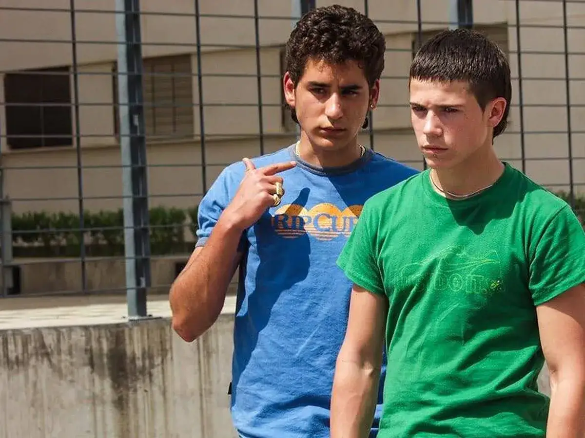 Dos jóvenes, uno con camiseta azul y otro con verde, posan. La edad de Juan José Ballesta se intuye en su rostro juvenil.