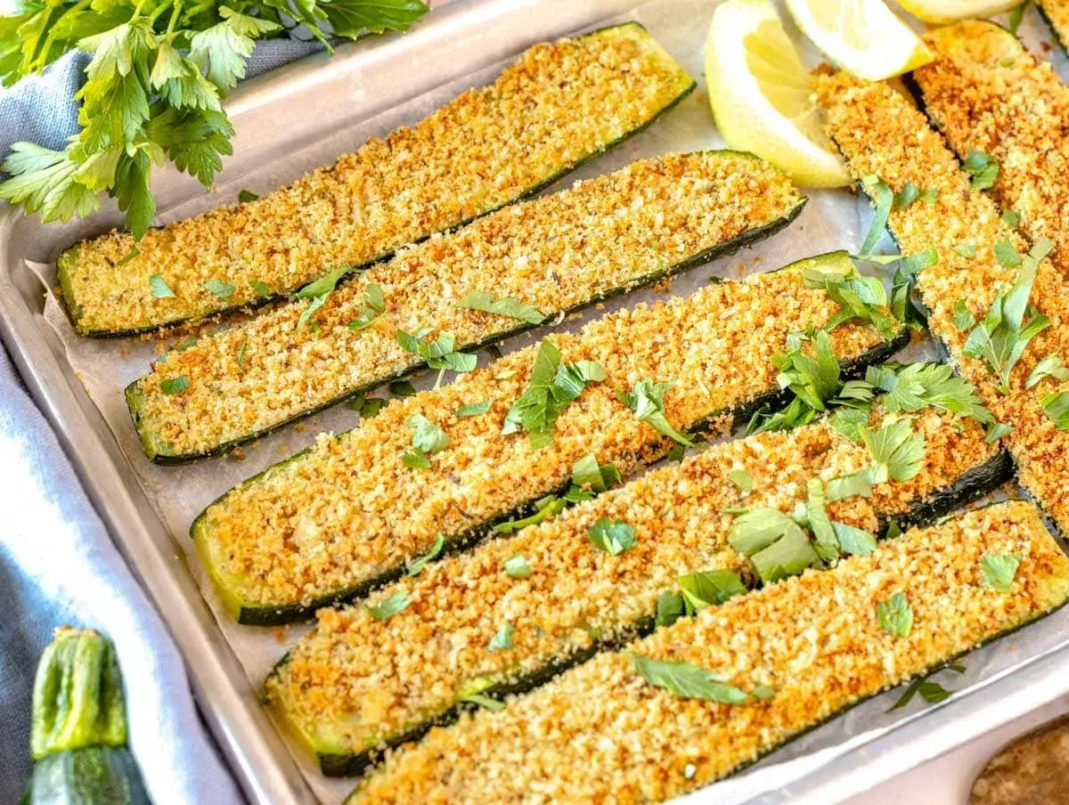 Calabacín al horno crujiente, cortado en bastones y espolvoreado con pan rallado y perejil fresco. Servido con gajos de limón.