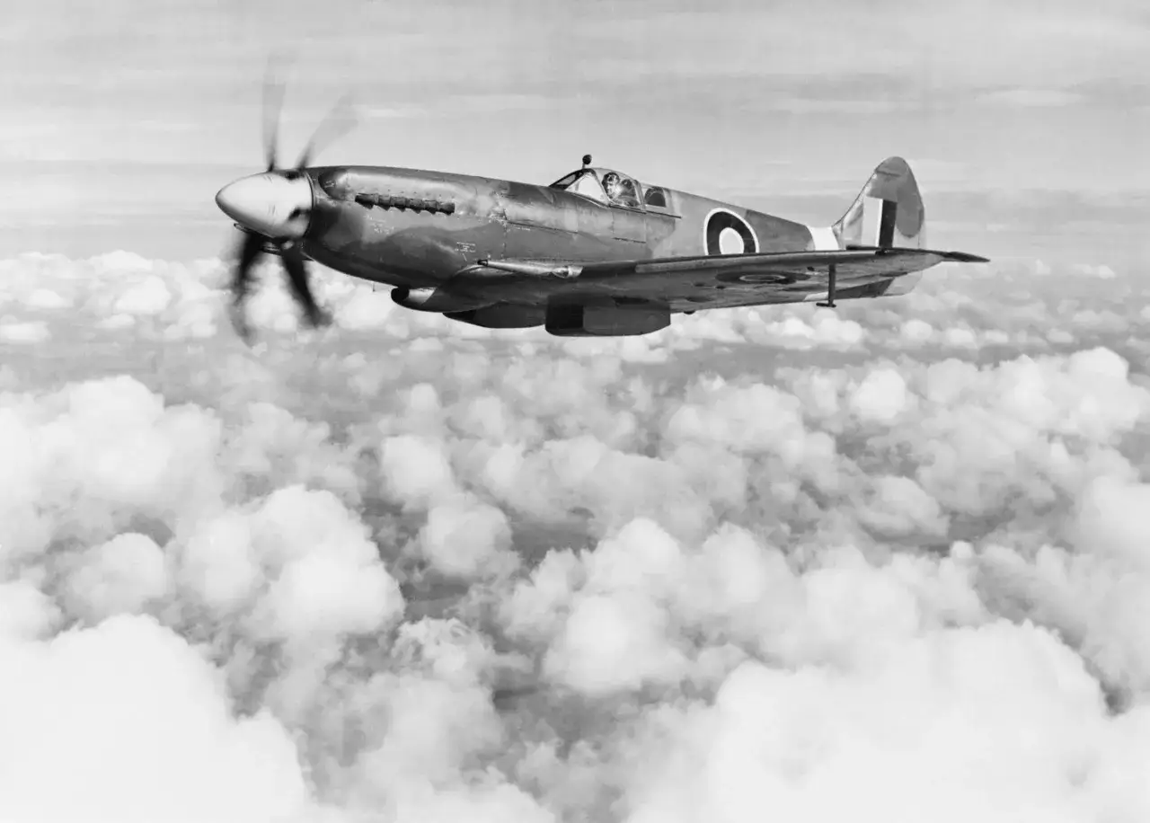 Ein Spitfire Flugzeug fliegt über den Wolken. Der Pilot ist im Cockpit zu sehen.