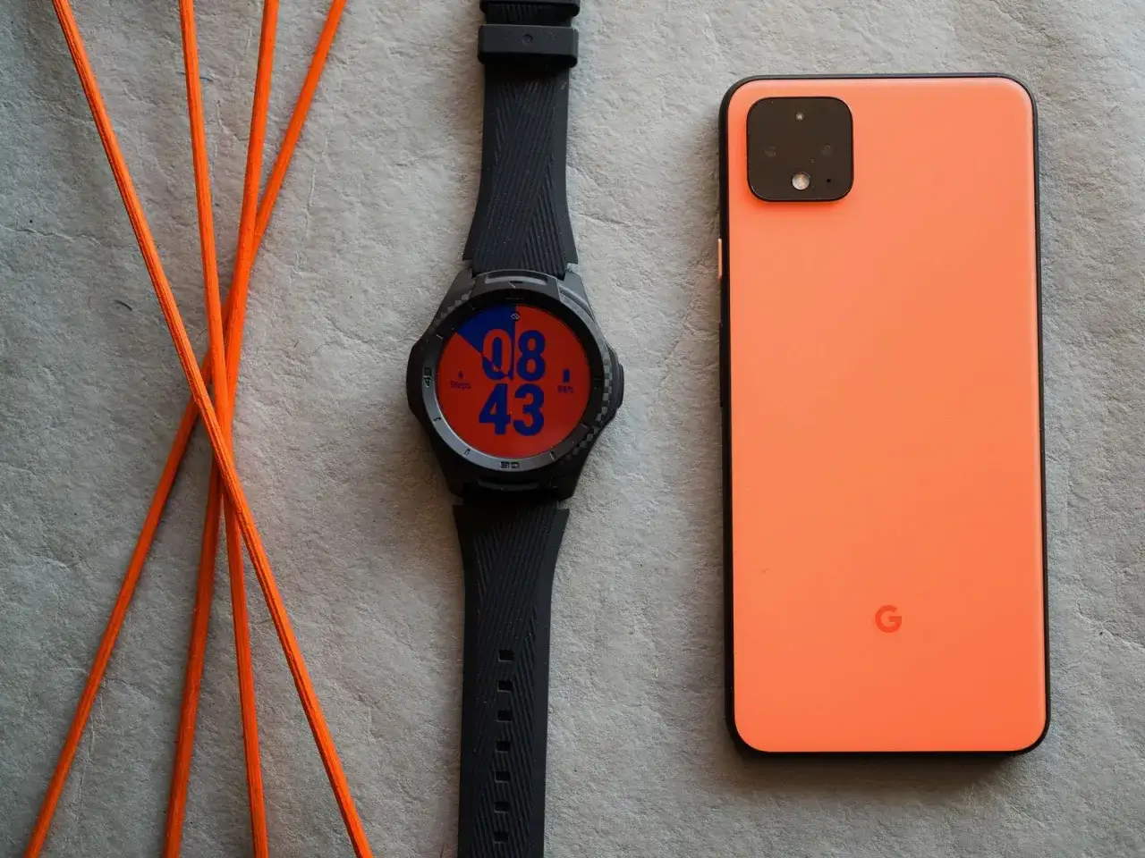 Zegarek z systemem Wear OS obok pomarańczowego telefonu.