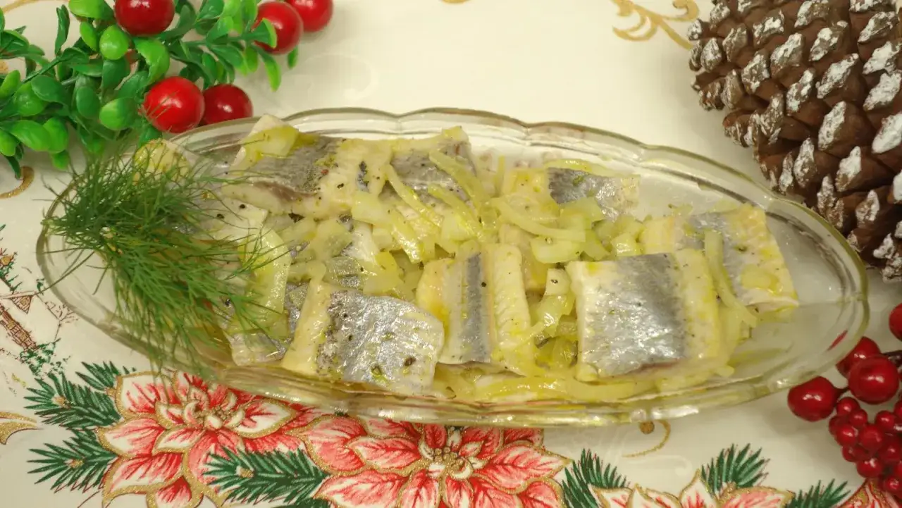 Pyszne śledzie z cebulką w oleju, udekorowane gałązką koperku, na świątecznym obrusie.