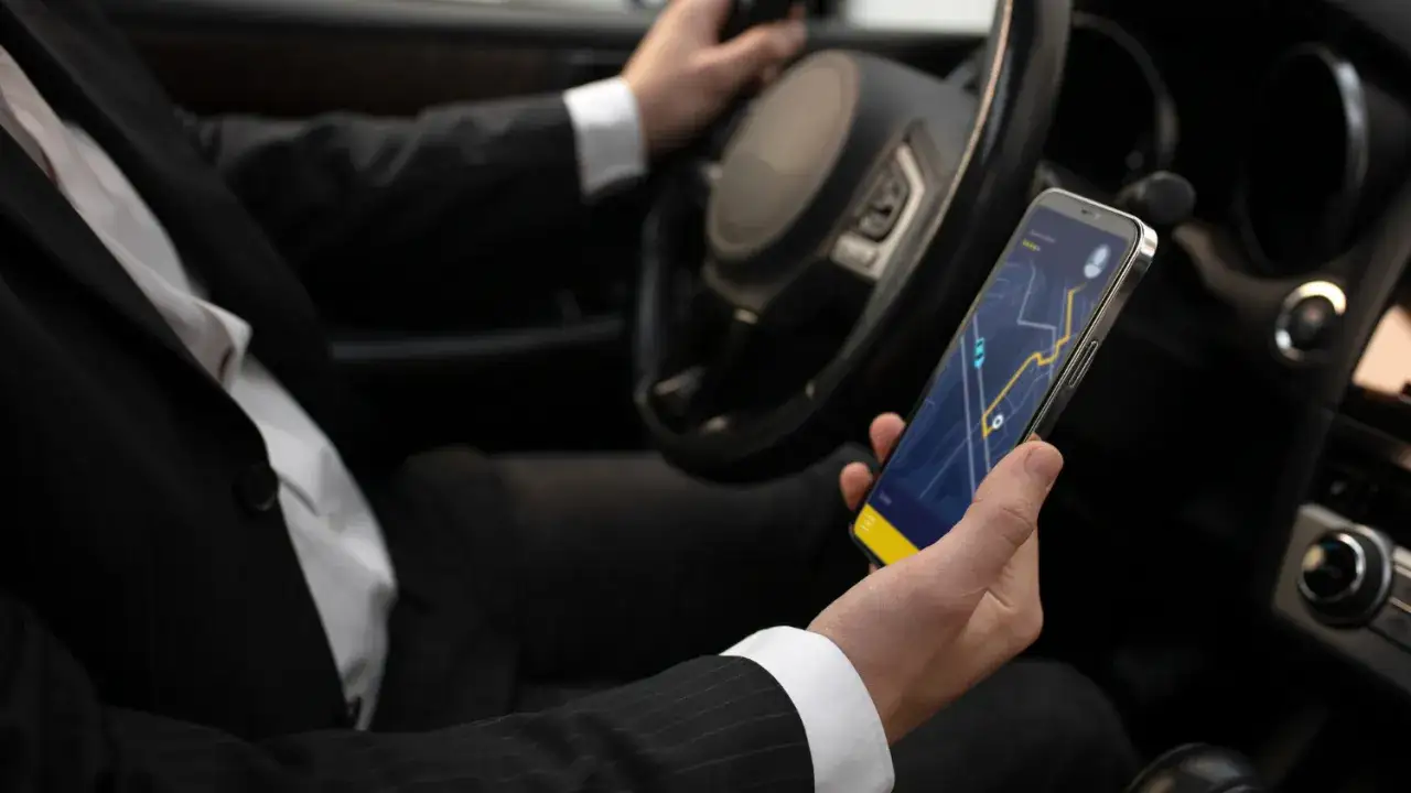 Kierowca w garniturze trzyma smartfon z mapą nawigacji, kt&oacute;ra działa jak wirtualna kasa fiskalna taxi.