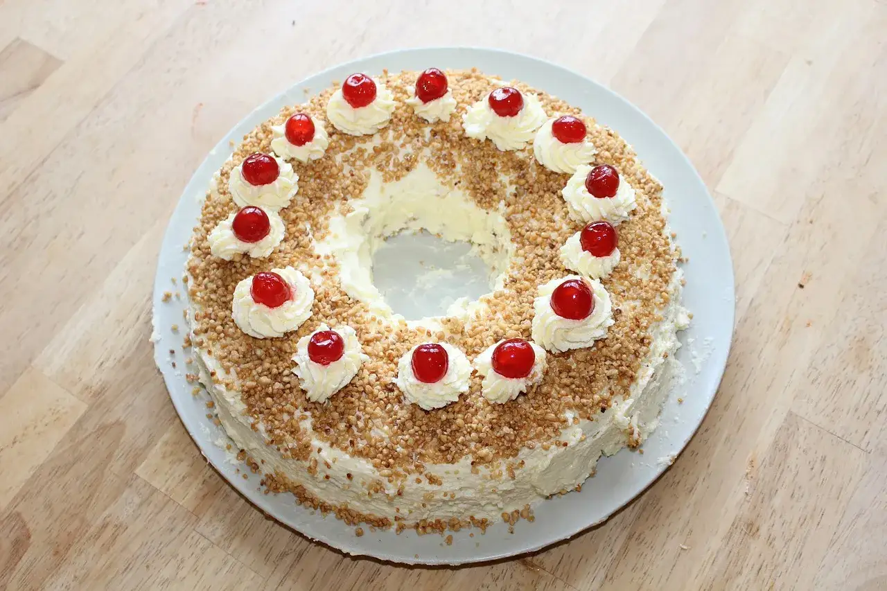 Ein Kranzkuchen mit Sahnetuffs und Kirschen, umh&uuml;llt von gehackten N&uuml;ssen. Perfekt f&uuml;r die besten Torten Rezepte!