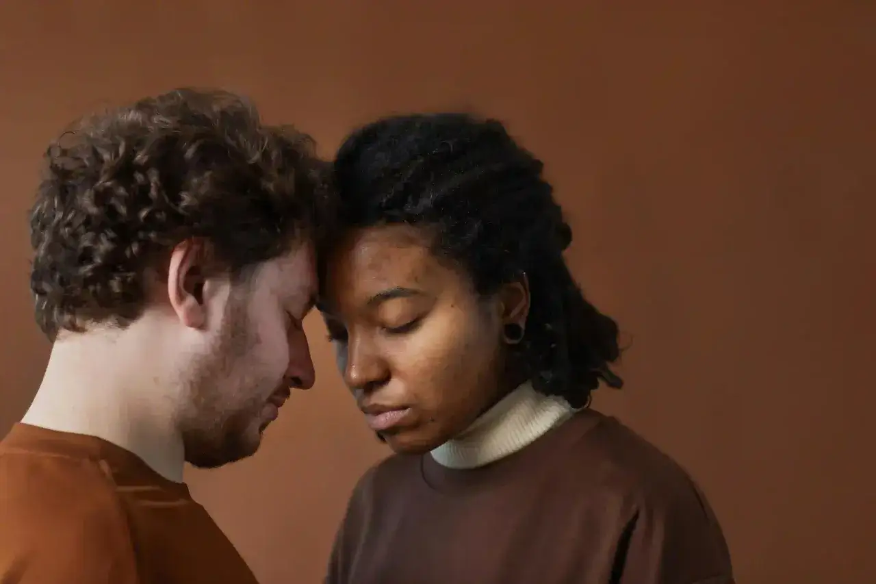 Coppia con fronti uniti, occhi chiusi, in un momento di riflessione. Lei ha la pelle scura, lui chiara. Potrebbe esserci un dialogo silenzioso sui dubbi sulla sessualità di mio marito.
