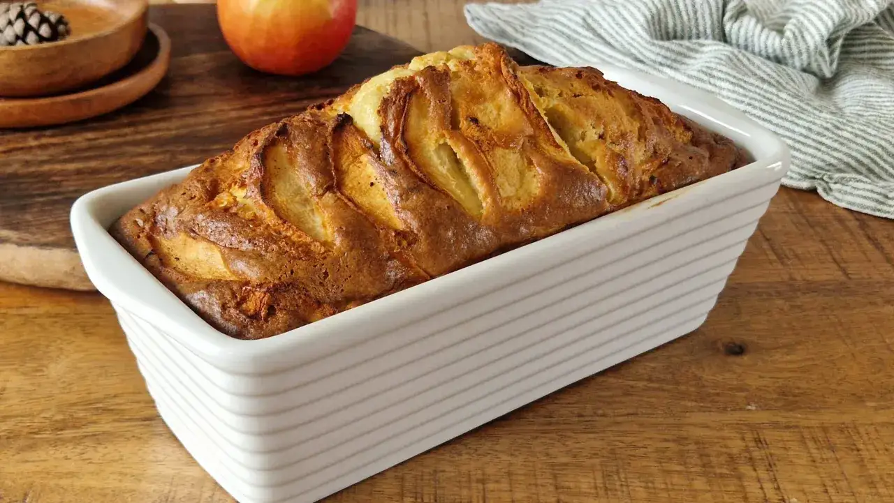 Un d&eacute;licieux clafoutis aux pommes tout juste sorti du four, dans son plat blanc, sur une table en bois.