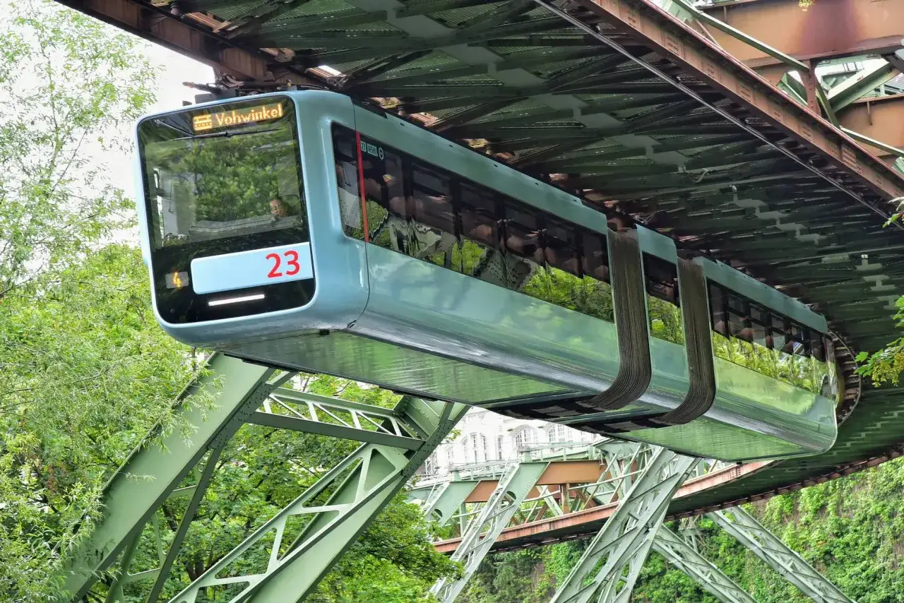 Der Schwebodrom Wuppertal: Eine hellblaue Schwebebahn f&auml;hrt auf ihrer Trasse durch &uuml;ppiges Gr&uuml;n.