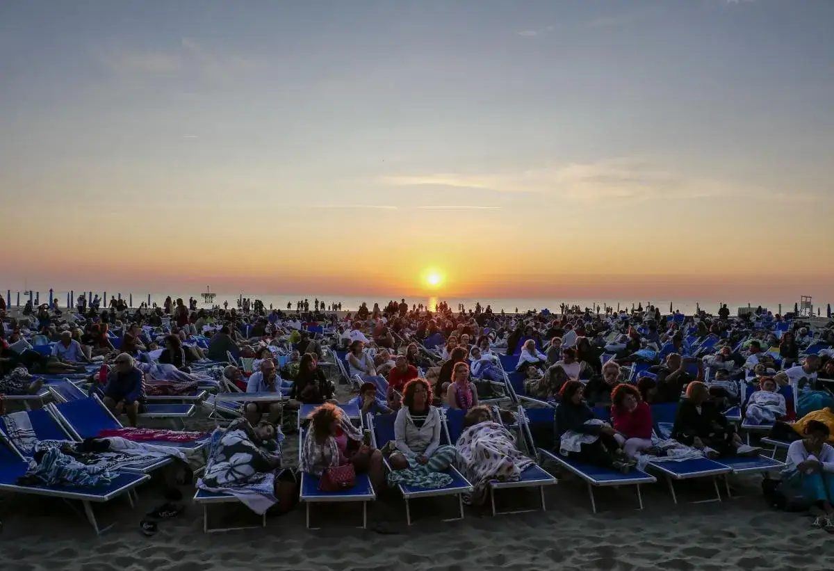 Folla di persone sedute su lettini in spiaggia al tramonto, per la Notte Rosa di Riccione.