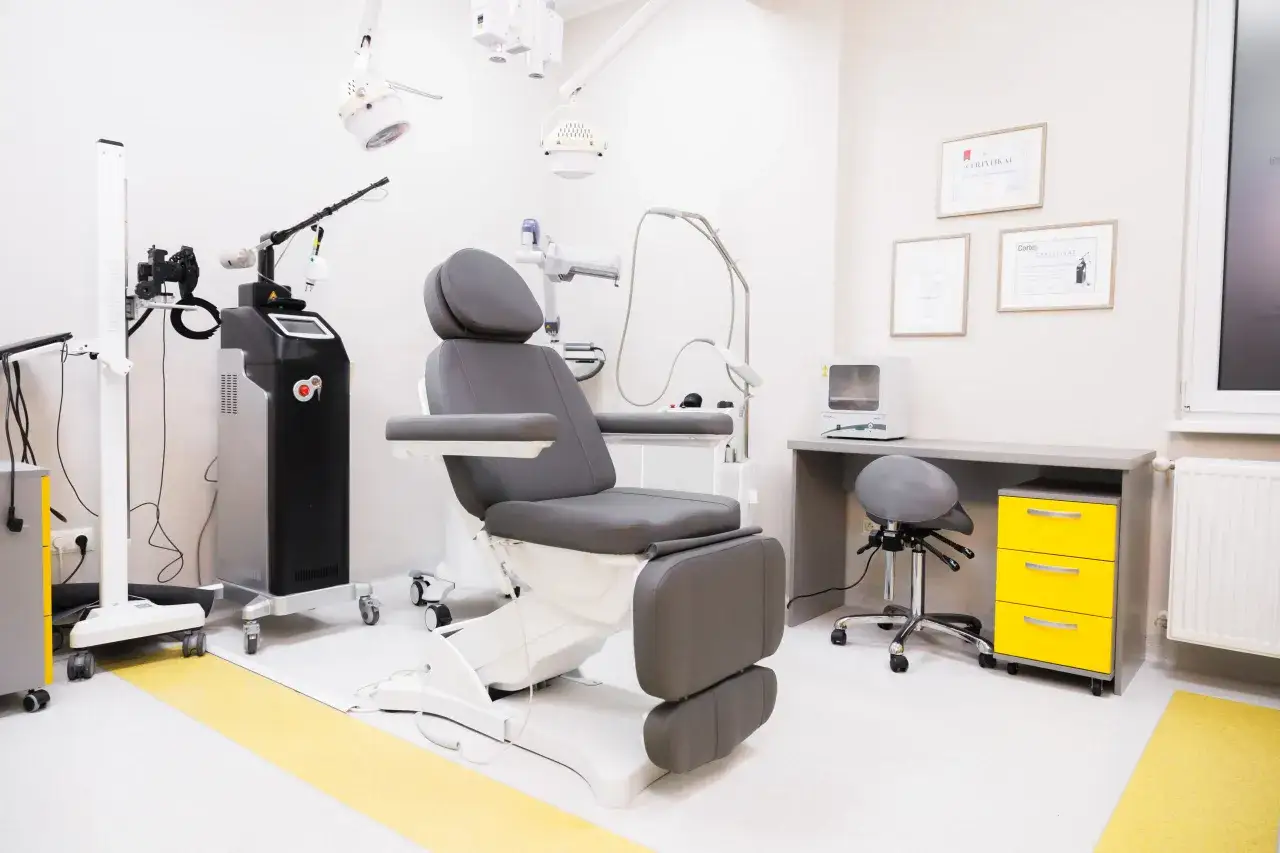 Gabinet dermatologii estetycznej z fotelem zabiegowym, laserem i certyfikatami na ścianie.