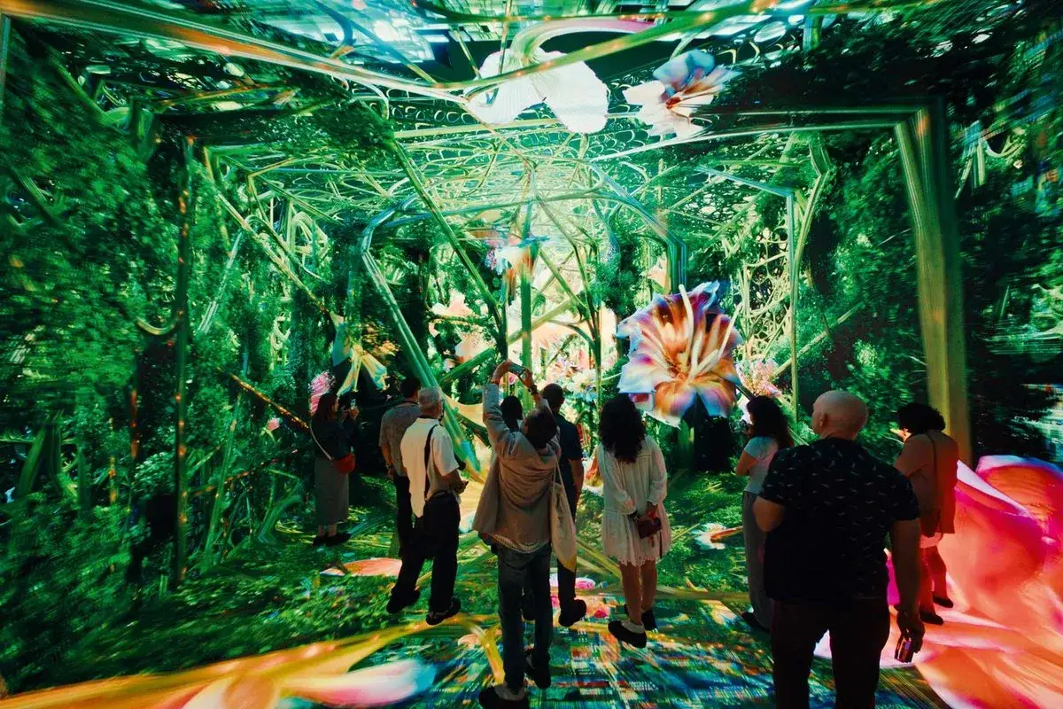 Visitors explore an immersive digital forest at the Los Angeles Center for Digital Art, surrounded by vibrant projections of giant flowers and lush greenery.