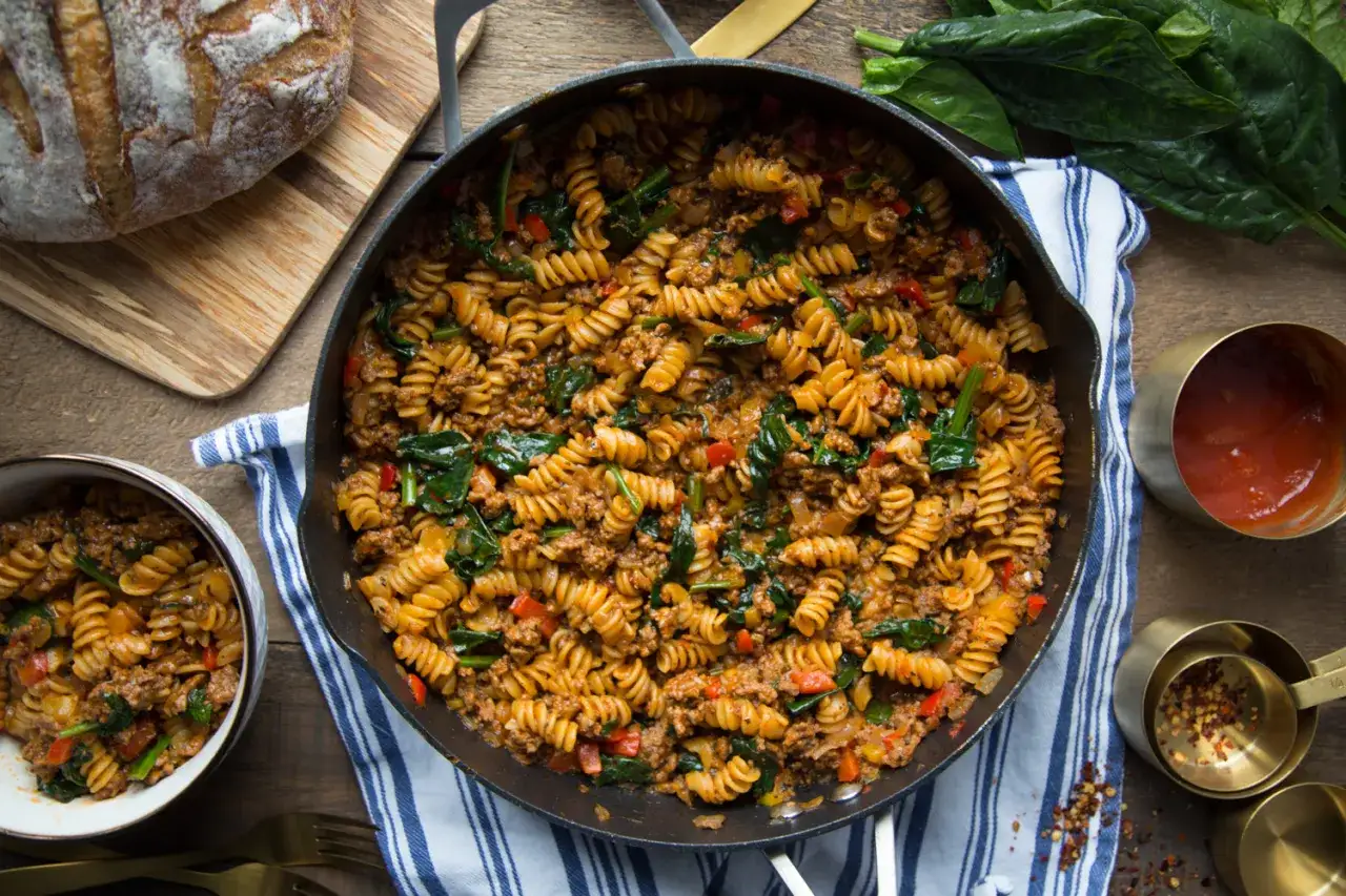 Un plat g&eacute;n&eacute;reux de p&acirc;tes &agrave; la viande, avec des fusillis, des &eacute;pinards et des poivrons, servi dans une po&ecirc;le en fonte.