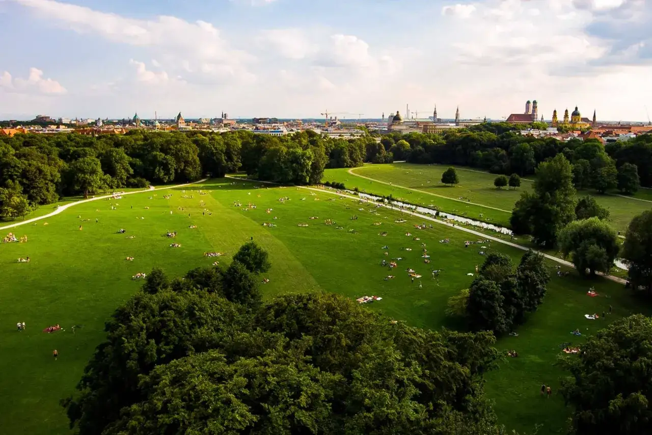 Zielony park w Monachium, gdzie ludzie odpoczywają na trawie. W tle widać panoramę miasta, idealne miejsce, by zobaczyć, co zwiedzić w Monachium.