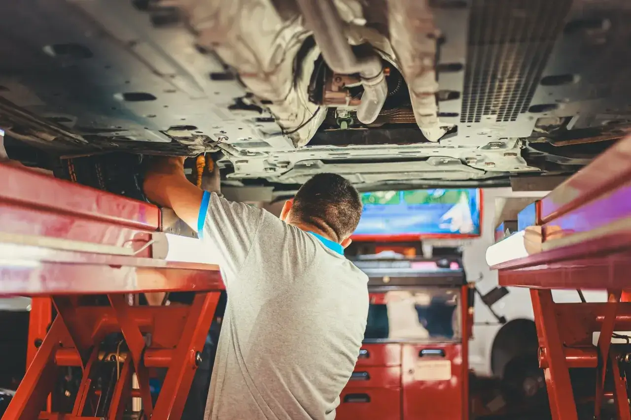 Mechanik pracuje pod samochodem, wykonując wymianę sworznia wahacza.